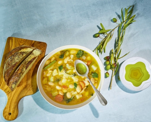 Bowl of bean suup with plate of olive oil, olive sprigs, and bread on cutting board