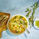 Bowl of bean suup with plate of olive oil, olive sprigs, and bread on cutting board