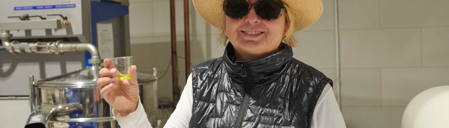 Woman in straw hat and sunglasses holding small glass with olive oil