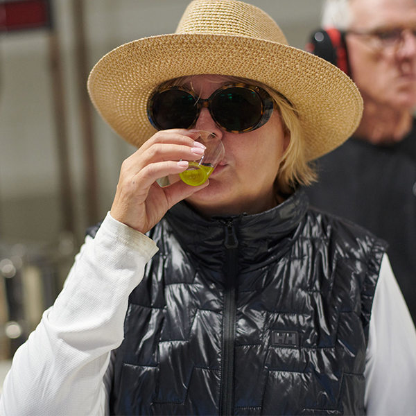 Woman in straw hat and sunglasses taking sip of olive oil from a small cup